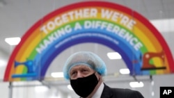 Britain's Prime Minister Boris Johnson, wearing a face mask to prevent the spread of the coronavirus, visits a PPE manufacturing facility during a visit to the north east of England, in Seaton Delaval, England, Saturday, Feb. 13, 2021. (AP Photo…