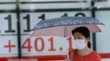 A woman wearing a face mask walks by an electronic stock board of a securities firm in Tokyo, Monday, Aug. 3, 2020. Asian shares were mixed on Monday, as investors watched surging numbers of new coronavirus cases in the region, including in Japan. …