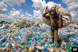 FILE - A man walks on a mountain of plastic bottles as he carries a sack of them to be sold for recycling after weighing them at the dump in the Dandora slum of Nairobi, Kenya, Dec. 5, 2018.