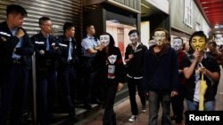 Demonstran pro-demokrasi yang menggunakan topeng Guy Fawkes melewati polisi di distrik Mongkok, Hong Kong (5/11). (Reuters/Bobby Yip)