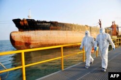 Petugas inspeksi imigrasi China dengan pakaian pelindung berjalan melewati sebuah kapal tanker minyak di sebuah pelabuhan di Qingdao, di provinsi Shandong timur China.  (Foto: AFP)