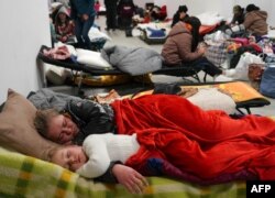 Refugiados de Ucrania descansan mientras esperan el transporte a otros destinos, el 4 de marzo de 2022 en un centro comercial vacío en Przemysl, Polonia. - Más de un millón de personas han huido de Ucrania a los países vecinos desde que Rusia lanzó su invasión a gran escala hace apenas una semana. (Foto de JANEK SKARZYNSKI / AFP)