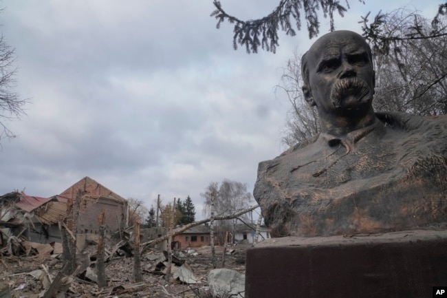 Patung Taras Shevchenko, penyair dan simbol nasional Ukraina, berdiri dengan latar belakang rumah budaya yang hancur setelah serangan udara malam di vVllage of Byshiv, 40 kilometer barat Kyiv, Ukraina, Jumat, 4 Maret 2022. (Foto: : AP/Efrem Lukatsky)
