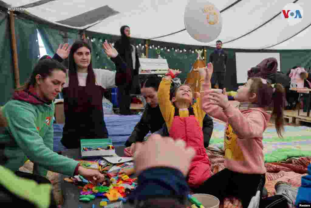 Niños juegan mientras se refugian dentro de una tienda de campaña con otras personas.