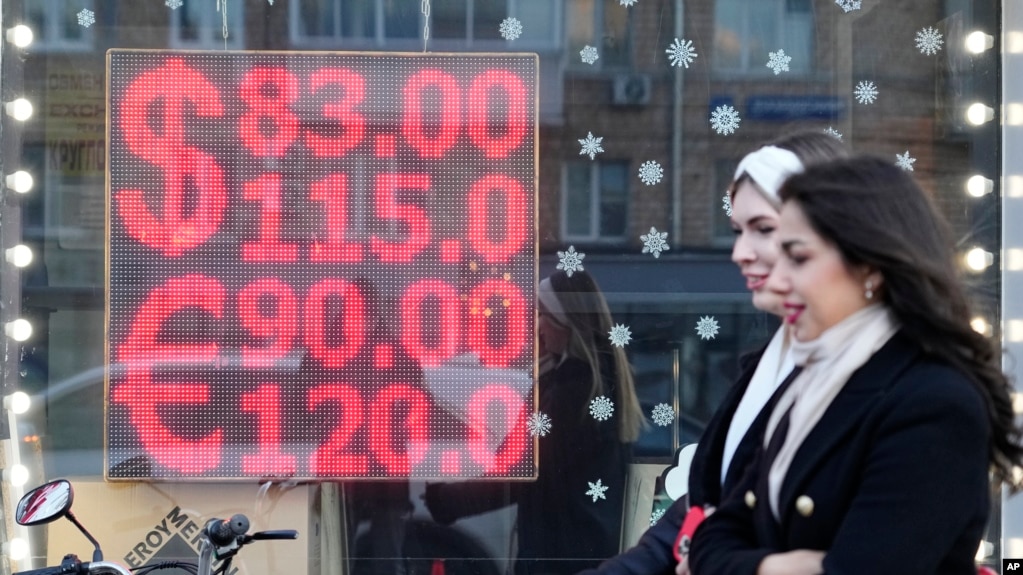 People walk past a currency exchange office screen displaying the exchange rates of U.S. Dollar and Euro to Russian Rubles in Moscow's downtown, Russia, Monday, Feb. 28, 2022. (AP Photo/Pavel Golovkin)