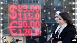 People walk past a currency exchange office screen displaying the exchange rates of U.S. Dollar and Euro to Russian Rubles in Moscow's downtown, Russia, Monday, Feb. 28, 2022. (AP Photo/Pavel Golovkin)