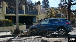 A stranded car sits next to a burned building near the Palisades Fire zone in the aftermath of a storm in the Pacific Palisades neighborhood of Los Angeles, California, Feb. 14, 2025.