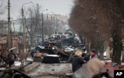 Orang-orang melihat reruntuhan kendaraan militer Rusia di sebuah jalan di kota Bucha, dekat ibu kota Kyiv, Ukraina, Selasa, 1 Maret 2022. (Foto: AP)