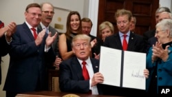 President Donald Trump shows an executive order on health care that he signed in the Roosevelt Room of the White House, Oct. 12, 2017, in Washington.