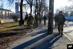 ARCHIVO - Soldados ucranianos patrullan un área no lejos de camiones militares en llamas en una calle de Kiev, Ucrania, el 26 de febrero de 2022. Según informes, más de 3.000 voluntarios estadounidenses se dirigen a Ucrania para ayudar a sus soldados a luchar contra el ejército invasor ruso.