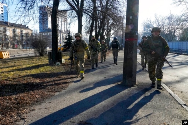 ARCHIVO - Soldados ucranianos patrullan un área no lejos de camiones militares en llamas en una calle de Kiev, Ucrania, el 26 de febrero de 2022. Según informes, más de 3.000 voluntarios estadounidenses se dirigen a Ucrania para ayudar a sus soldados a luchar contra el ejército invasor ruso.