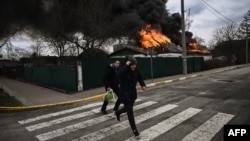 People run for cover in front of a burning house during shelling in the city of Irpin, outside Kyiv, on March 4, 2022.