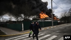 Dos personas corren por una calle de Irpin, en las afueras de Kiev, Ucrania, frente a un edificio incendiado por la artillería rusa el 4 de marzo de 2022.