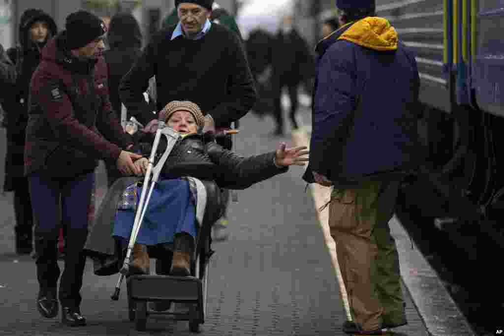 Varios hombres empujan un carrito de equipaje que transporta a una anciana antes de abordar un tren con destino a Lviv, en Kiev, Ucrania, el jueves 3 de marzo de 2022.