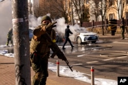 Tentara Ukraina mengambil posisi di luar fasilitas militer saat dua mobil terbakar, di sebuah jalan di Kyiv, Ukraina, Sabtu, 26 Februari 2022. (Foto: AP)