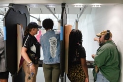 In this Aug. 21, 2021, image taken from video, firearms instructors, left, and right, teach female customers on the shooting range at the Recoil Firearms store in Taylor, Mich.