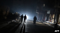 FILE - A group of men walk down a street without electricity late in the besieged rebel bastion of Douma, northeast of the Syrian capital Damascus on Nov. 10, 2014.