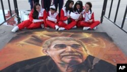 FILE - Students read guides to Bogota's International Book Fair, as they sit next to a chalk painting of the late Colombian novelist Gabriel Garcia Marquez, in Bogota, Colombia, April 28, 2015.
