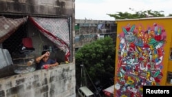 A drone view shows a boy watching outside his apartment next to a mural titled 'Outside,' in Mejicanos, El Salvador, July 18, 2024.