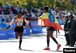 Meb Keflezighi of USA (L) gets a high five from Gebre Gebremariam of Ethiopia as Keflezighi runs for the finish line where he finished fourth in the men's professional division of the 2014 New York City Marathon in Central Park in Manhattan, Nov. 2, 2014.