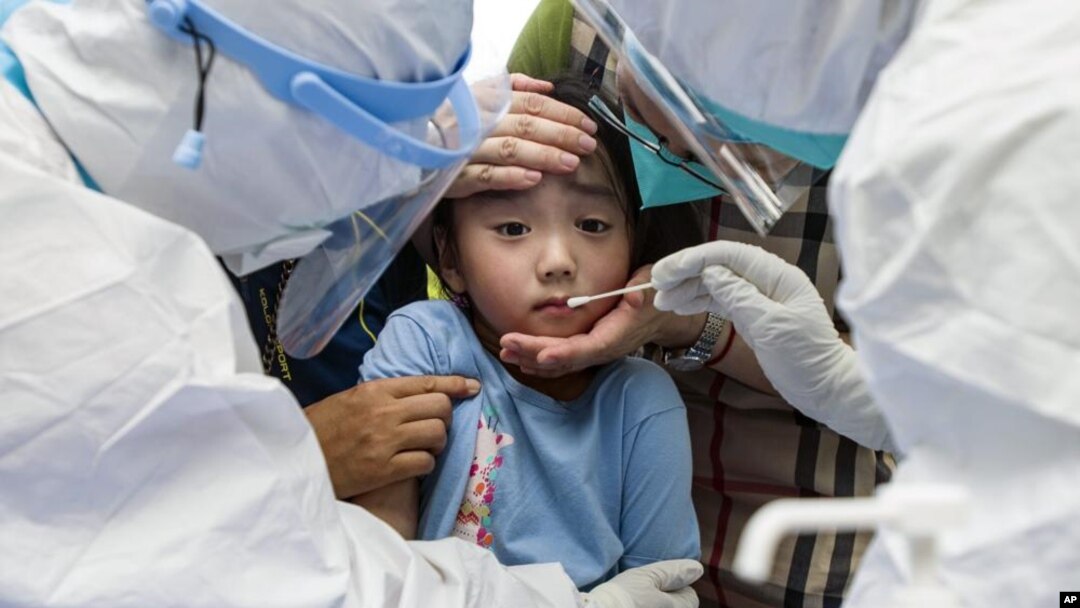A child reacts to a throat swab during mass testing for COVID-19 in Wuhan