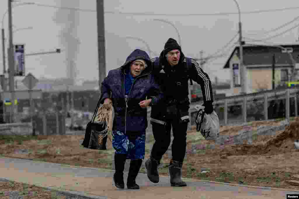 A man helps an elderly woman to run for cover after heavy shelling by Russian troops on the only escape route used by locals in Irpin, March 6, 2022.
