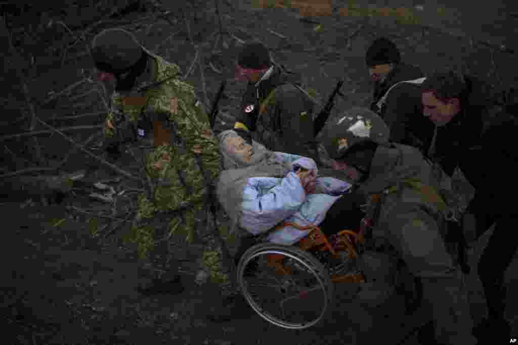 乌克兰军人和民兵帮助一名坐在轮椅上的老妇人撤离，附近仍有炮火声。（2022年3月7日）