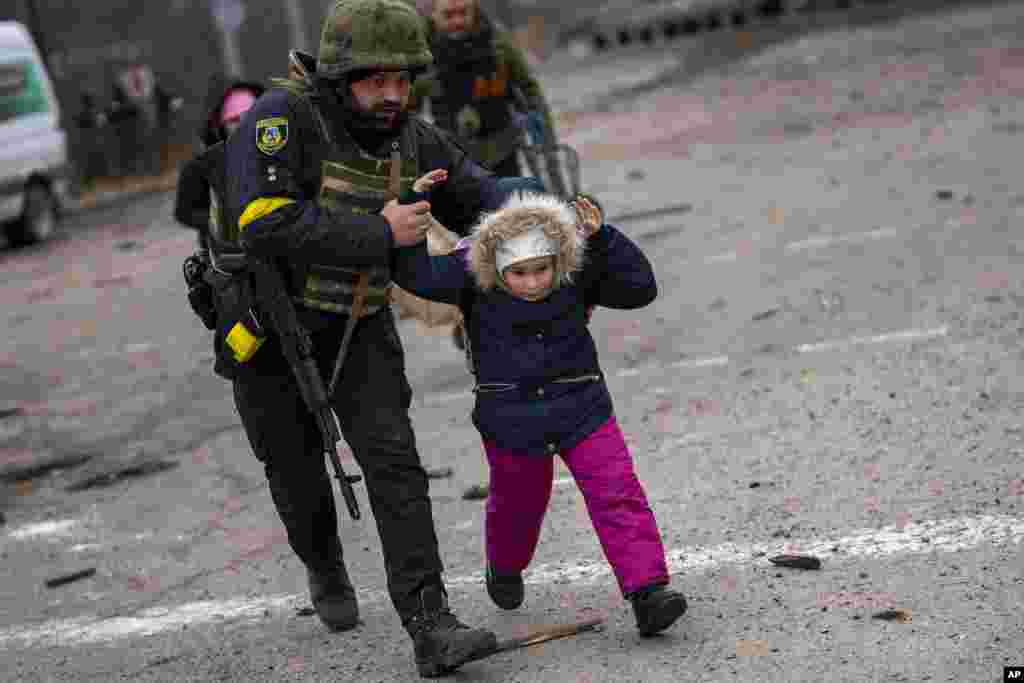 一名乌克兰军人掩护一名儿童逃离伊尔平，远处传来炮火声。（2022年3月7日）
