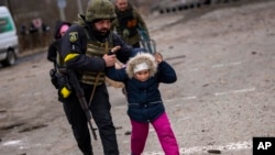 A Ukrainian police officer runs while holding a child as the artillery echoes nearby, while fleeing Irpin on the outskirts of Kyiv, March 7, 2022.