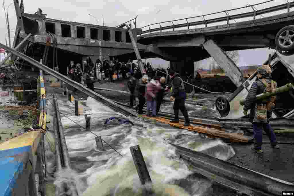 Os residentes atravessam uma ponte destruída ao evacuarem da cidade de Irpin, após dias de fortes bombardeamentos na única rota de fuga, enquanto as tropas russas avançavam em direcção à capital Kyiv, Ucrânia, 7 de Março de 2022.