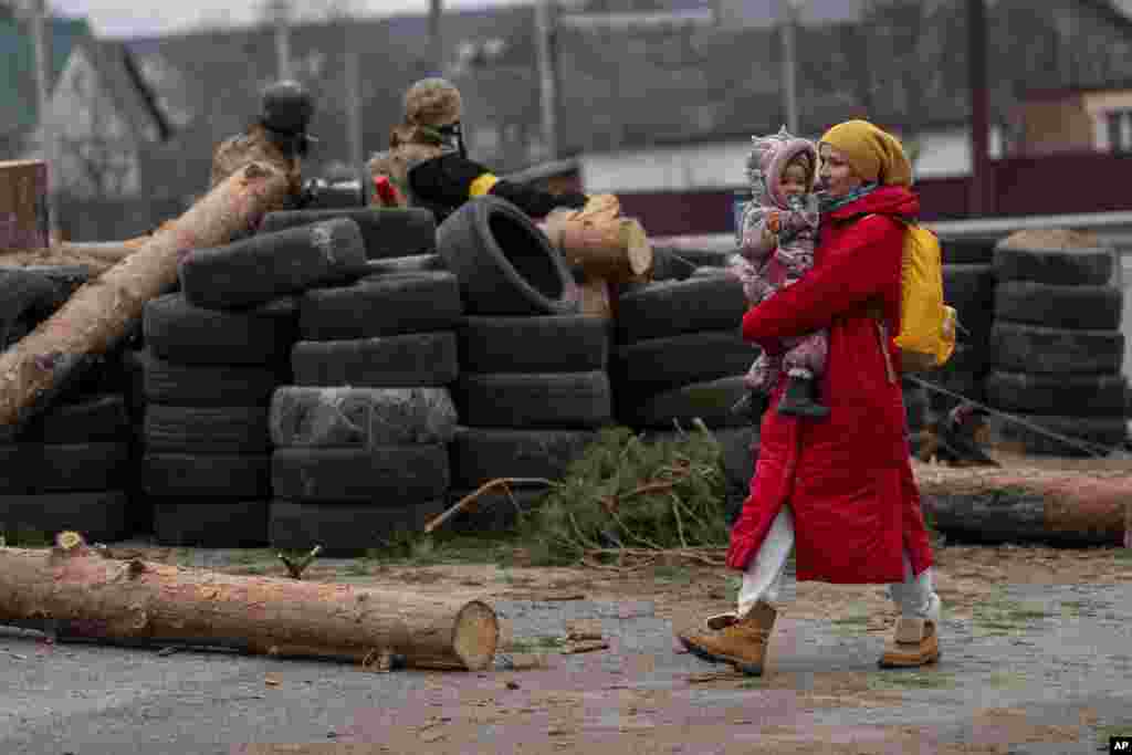 Una mujer ucraniana con un bebé en brazos pasa frente a una barricada controlada por soldados ucranianos mientras huyen cruzando el río Irpin en las afueras de Kiev, Ucrania.