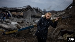 A woman rests after crossing a destroyed bridge as she evacuates from the city of Irpin, northwest of Kyiv, on March 7, 2022.