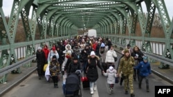 Ukrainian refugees walk a bridge at the buffer zone with the border with Poland in the border crossing of Zosin-Ustyluh, western Ukraine, March 6, 2022.