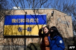 FILE - People walk past signage in the design of Ukraine's national flag with the message "We Support Ukraine" outside the Canadian embassy in Beijing, March 3, 2022.