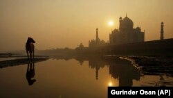 A stray dog pauses on a sand bank of the Yamuna River as the sun is seen rising over the Taj Mahal in Agra, India. The white-marble monument to love was built by the Mogul Emperor Shah Jahan between 1632 and 1654 for his favorite wife, Mumtaz Mahal.