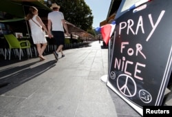 A couple walk through the empty flower market in the old city and near a sign which reads, "Pray for Nice" days after a truck attack on the Promenade des Anglais on Bastille Day killed scores and injured as many in Nice, France, July 17, 2016.