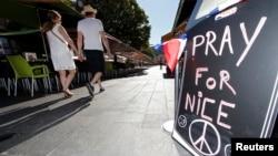 A couple walk through the empty flower market in the old city and near a sign which reads, "Pray for Nice" days after a truck attack on the Promenade des Anglais on Bastille Day killed scores and injured as many in Nice, France, July 17, 2016. 