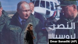 A woman passes a billboard showing Russian President Vladimir Putin in Damascus, Monday, March 7, 2022. The Arabic poster reads "The victory for Russia." (Omar Sanadiki/AP)