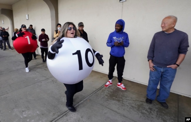 Dressed as Lotto balls, California Lottery employees Marina Maldonado, right, and Liza Solis, left, dance past people waiting to buy Powerball tickets at Lichine's Liquor & Deli in Sacramento, Calif., Nov. 7, 2022. (AP Photo/Rich Pedroncelli)