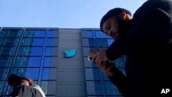 FILE - People walk outside Twitter headquarters in San Francisco, Nov. 4, 2022. Since Elon Musk acquired Twitter two weeks ago, the company has offered, then paused, a new blue check subscription service.
