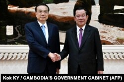 លោក​នាយករដ្ឋមន្ត្រី ហ៊ុន សែន (ស្ដាំ) និង​នាយករដ្ឋមន្ត្រី​ចិន​លោក Li Keqiang ចាប់​ដៃ​គ្នា​នៅ​វិមាន​សន្ដិភាព ក្នុង​រាជធានី​ភ្នំពេញ ថ្ងៃទី ៩ ខែវិច្ឆិកា ឆ្នាំ២០២២។ (Kok KY / CAMBODIA'S GOVERNMENT CABINET / AFP)