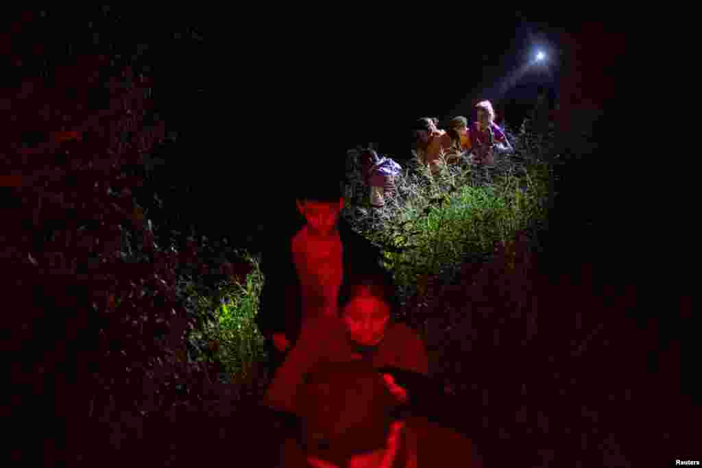 A border patrol agent lights a path for asylum seeking migrants from Central America as they navigate through thick brush after being smuggled from Mexico and across the Rio Grande river into Roma, Texas, Nov. 6, 2022. 