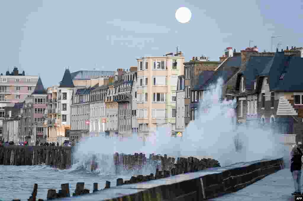 A wave crashes on the docks in Saint-Malo, France, as the moon rises.