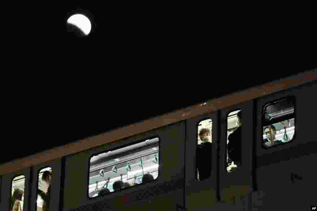 A lunar eclipse is seen over a commuter train in Tokyo, Japan, .