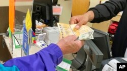 From behind the lottery counter at a Pick 'n Save store in Madison, Wis., Djuan Davis hands Powerball tickets to Arpad Jakab, on Nov. 5, 2022.