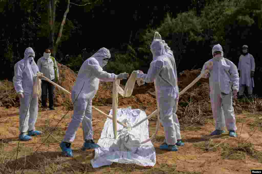 Relatives wearing protective gear prepare to bury the body of a man who died from the coronavirus disease (COVID-19), at a graveyard in New Delhi, India.