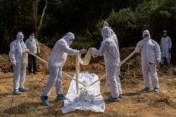 FILE - Relatives wearing protective gear prepare to bury the body of a man who died from the coronavirus disease, at a graveyard in New Delhi, India, April 14, 2020.