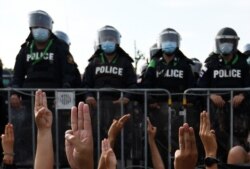 FILE - Protesters, facing riot police, flash the three-finger salute of defiance during an anti-government rally, outside the Government house in Bangkok, Thailand, March 30, 2021.