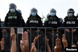 FILE - Protesters, facing riot police, flash the three-finger salute of defiance during an anti-government rally, outside the Government house in Bangkok, Thailand, March 30, 2021.