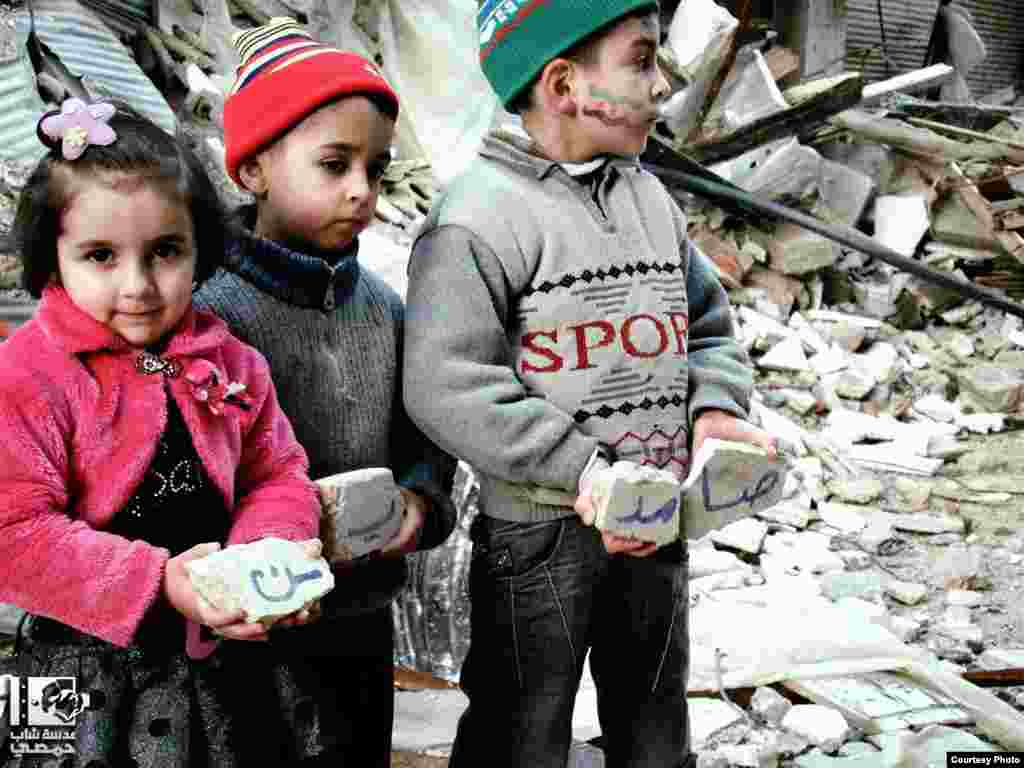 2013年1月10日，三名敘利亞兒童在霍姆斯端著從被炸毀的建築廢墟裡撿起的石頭。 (Lens Young Homsi)